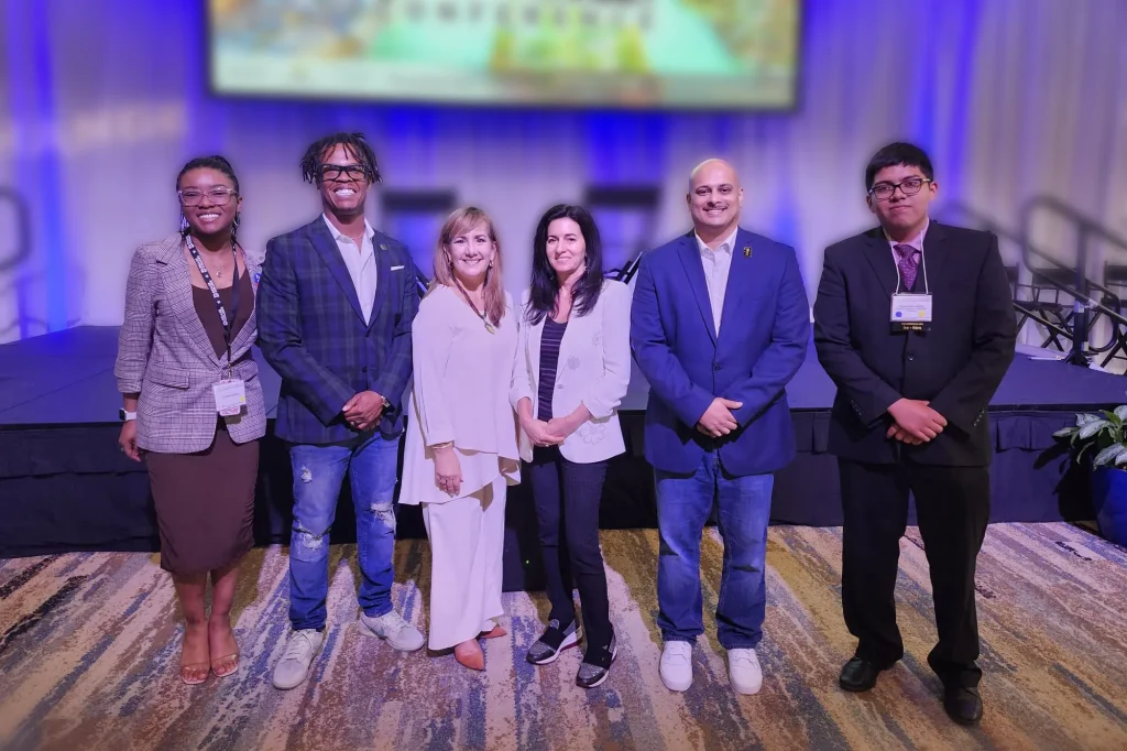 Monica Díaz standing on stage alongside a diverse panel of first-generation students and mentors at a business conference